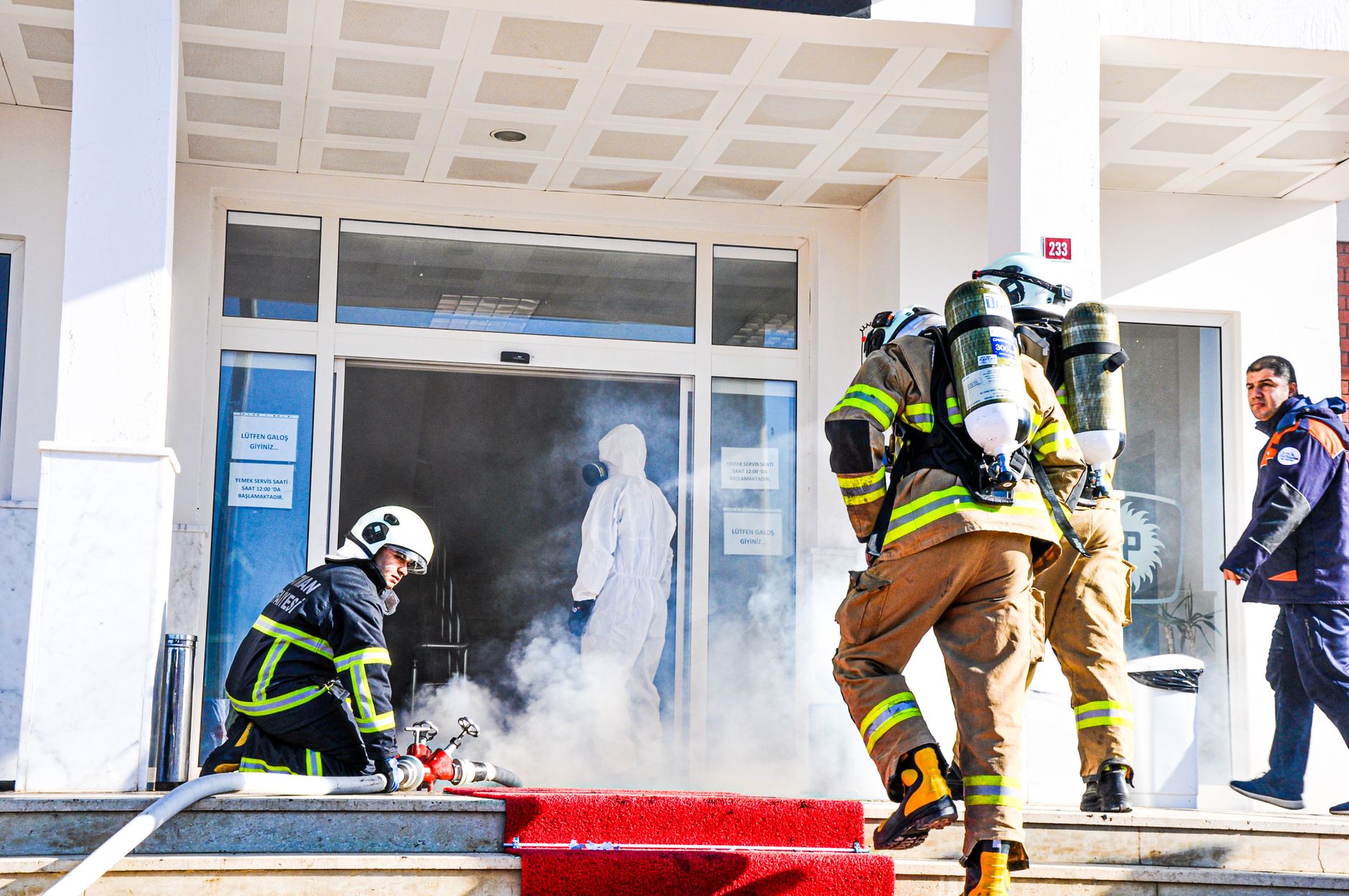 Firefighters responding to an emergency at a building entrance in Batman, Türkiye. Smoke and safety gear visible