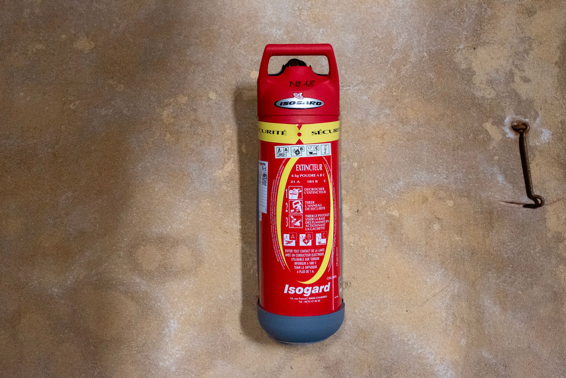 Red Isogard fire extinguisher mounted on a textured wall, focused view