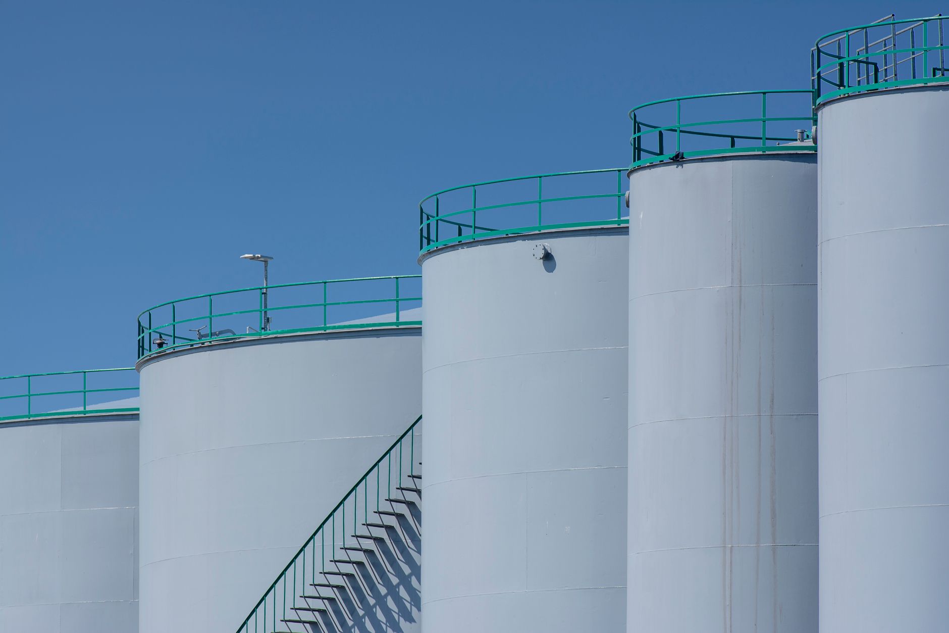 Large industrial storage tanks with green railings against a clear blue sky