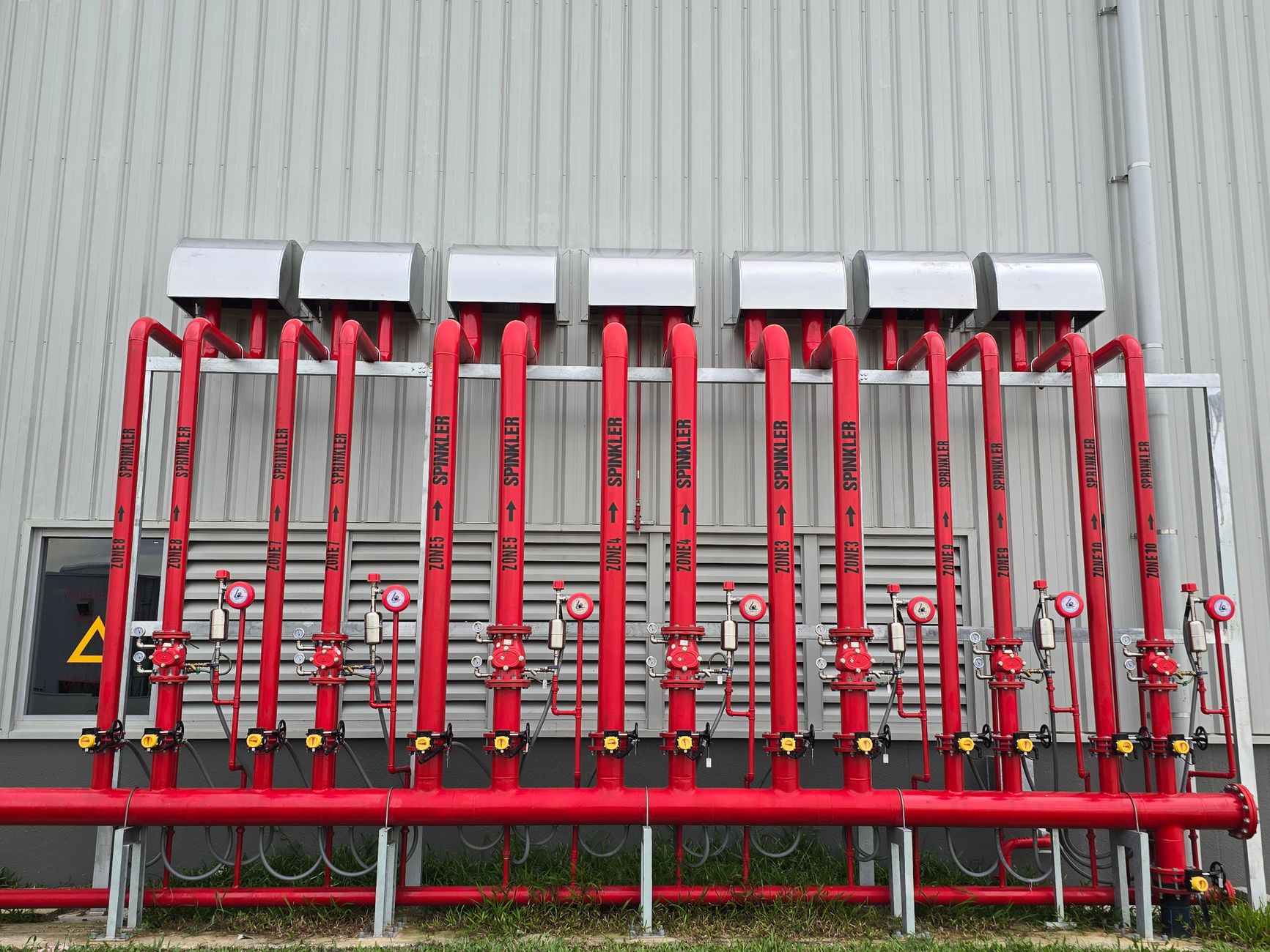 Red industrial fire sprinkler pipes aligned on a factory exterior wall