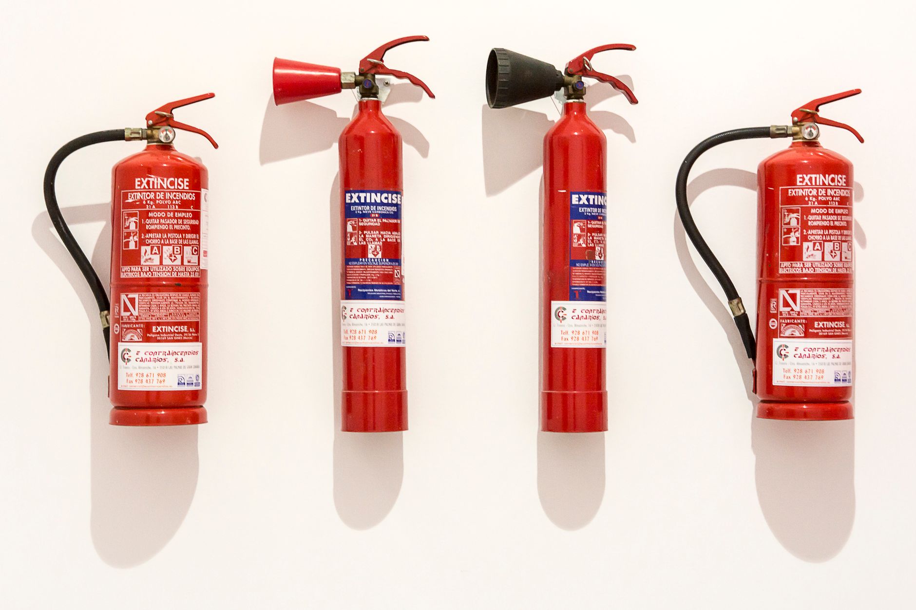 Four red fire extinguishers hanging on a clean white wall in an orderly fashion